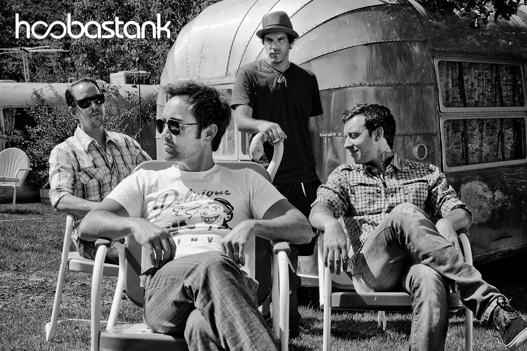 Hoobastank, three seated in lawn chairs and one standing, in front of a vintage aluminum trailer in Malibu, in black and white